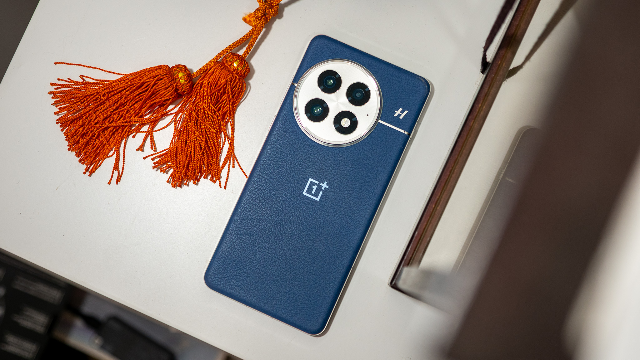 The back of the blue OnePlus 13 next to some orange tassels